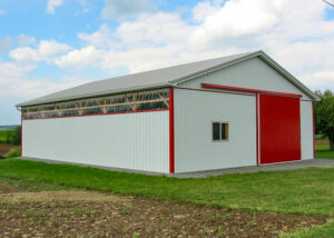 Post frame barn with white metal siding and red metal trim and doors